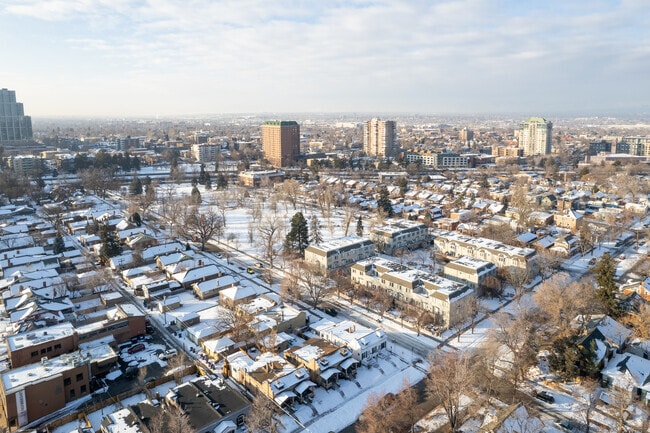 A serene winter morning blankets Alamo Placita in snow, contrasting cozy residential rooftops with the rising skyline beyond.
