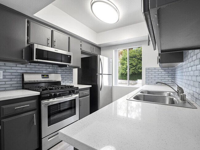 Tiled kitchen with stainless steel oven, microwave, and fridge.
