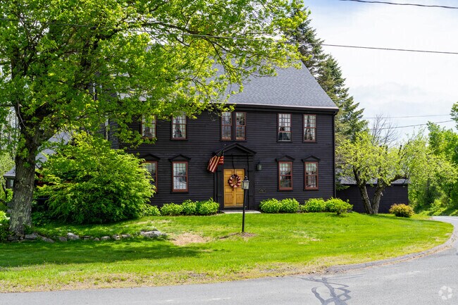 A black colonial style clapboard sided home sits on a corner of two main roads in Tolland.