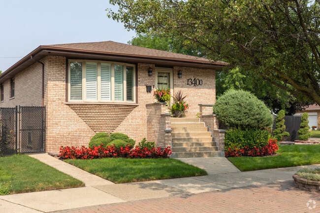 Tan brick bungalow home with red flowers and green grass, Hegewisch, Chicago, IL.