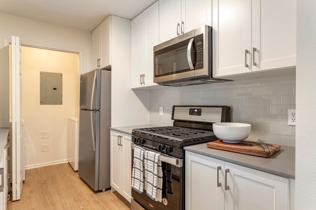 Renovated Package I kitchen with white cabinetry, grey quartz countertops, stainless steel appliances, hard surface flooring, and tile backsplash. In-unit washer and dryer