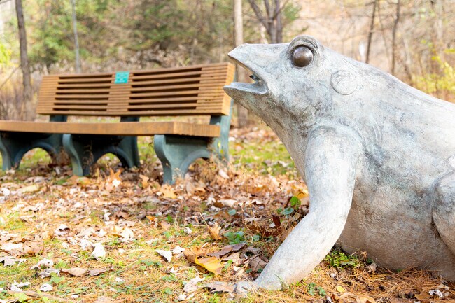A whimsical frog statue sits beside a bench along Fishing Creek in Pine Township.
