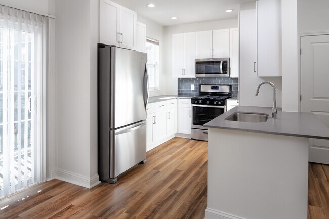 Kitchen with white cabinetry, grey quartz countertops, grey tile backsplash, stainless steel appliances, and hard surface flooring