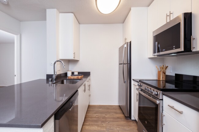 Renovated Package I kitchen with stainless steel appliances, dark grey quartz countertops, white cabinetry, and hard surface flooring