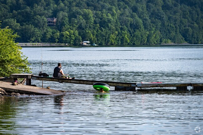 A father relaxes with a fishing pole as his son has fun in the water at Cheat Lake Park.