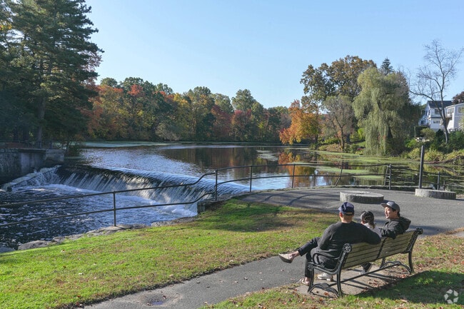 People sit on a park bench with views of the Charles River.