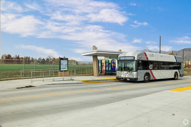 A bus stops at a modern bus stop with colorful glass panels at Weber State University.