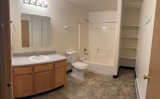Well-lit bathroom with a full tub/shower combo, extended vanity, and built-in shelving