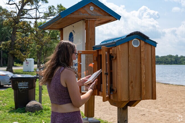 At Roller Rink Park, a young reader browses the outdoor book exchange, enjoying lakeside leisure in Bloomfield.