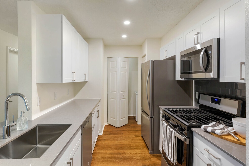 Renovated Package I kitchen with white cabinetry, grey quartz countertops, glass tile backsplash, and stainless steel appliances, and hard surface plank flooring