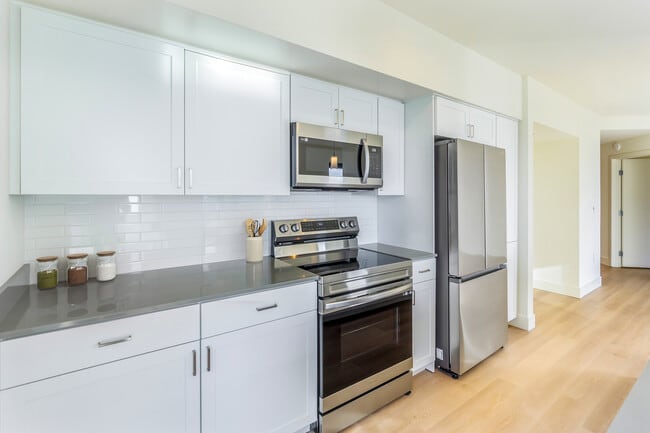 Renovated Package I kitchen with white cabinetry, grey quartz countertops, white subway tile backsplash, stainless steel appliances, and hard surface flooring