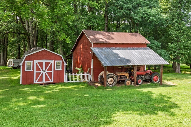 Classic red barn shelters vintage tractors beneath towering trees in Browns Summit.