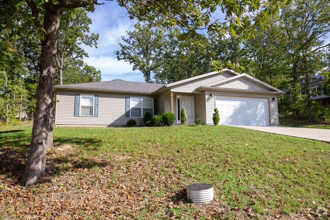 Charming single-story home with a two-car garage, nestled on a spacious lawn and framed by mature trees.