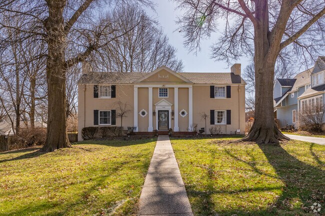 An older home sits framed by two large trees in a large front yard.