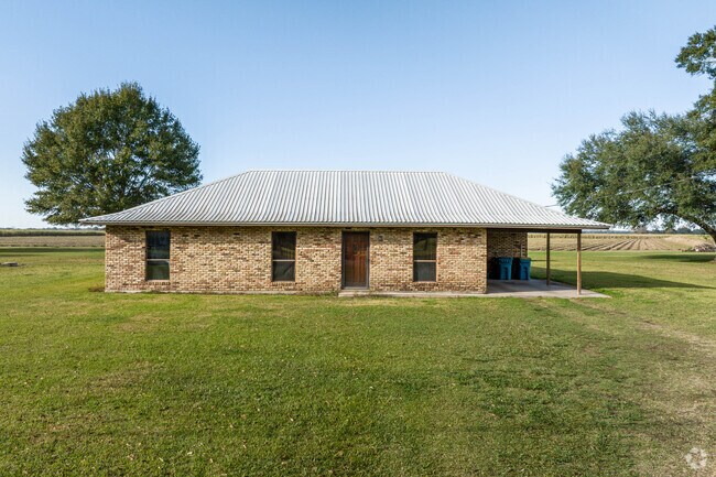 A single-story brick ranch-style home sits on a large plot of farmland in St Martinville, LA.