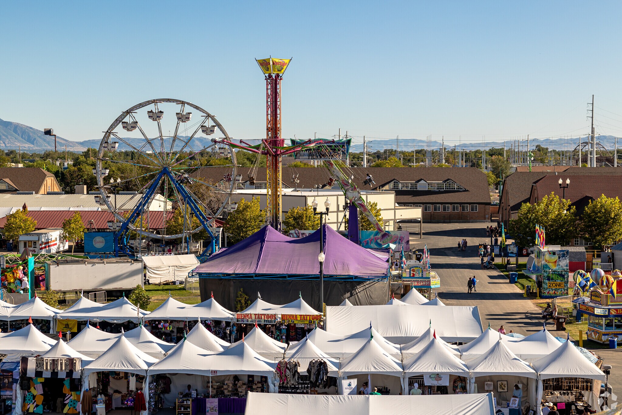 Rows of tented booths line the foreground with carnival rides in the background at Fairpark.