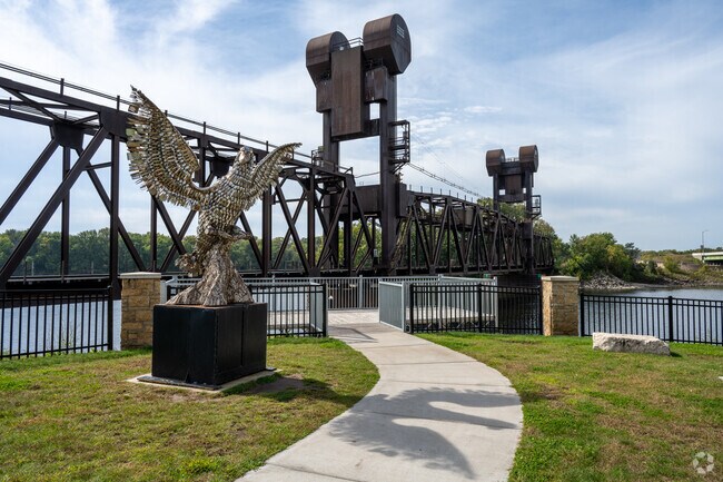 A bird statue, made from various kitchen utensils, stands in front of the Saint Croix Bridge.
