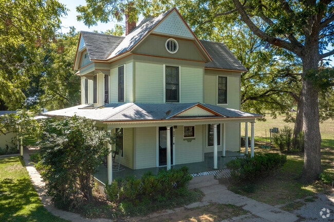 Large Victorian homes in Pilot Point are shaded by mature trees.