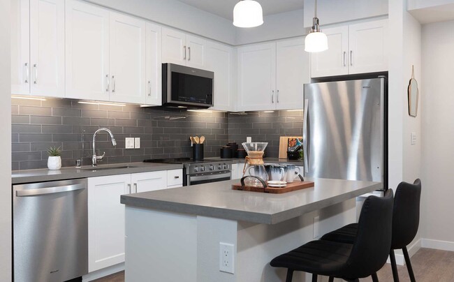 Upgrade Collection kitchen with stainless steel appliances, white cabinetry, grey quartz countertop, grey tile backsplash, and hard surface flooring