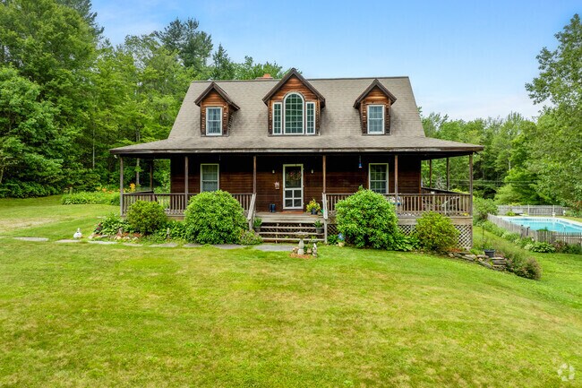 A cape-cod style home with stained wood siding is located far from the main roads along a dirt road.