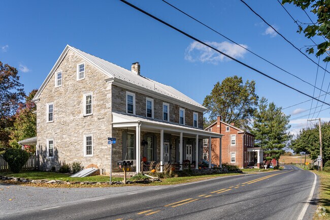 A large, stone colonial sits next to another brick version set right along a street in Millcreek