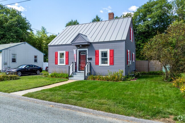 A grey cape style home in Maple Avenue District has red shutters and green lawn.