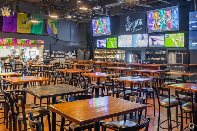 Inside of 115 Bourbon Street i a huge bar with multiple screens and a stage for live music.