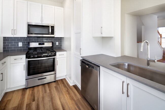 Kitchen with white cabinetry, grey quartz countertops, grey tile backsplash, stainless steel appliances, and hard surface flooring