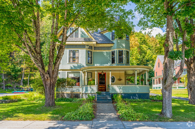 A Victorian style home in The Meadow has a large wraparound porch and is shaded by tall trees.