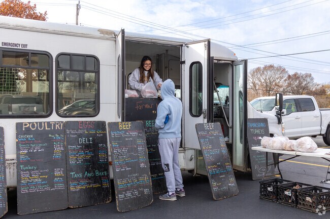 A farmer vendor brings farm-fresh meats and eggs from their bus to market shoppers outside.