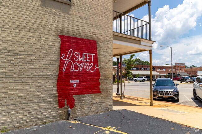 A red Alabama-shaped mural reading “Sweet Home Monroeville” decorates a brick wall in the town center.