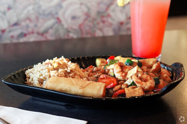 A delicious Chinese meal complete with an eggroll and juice.