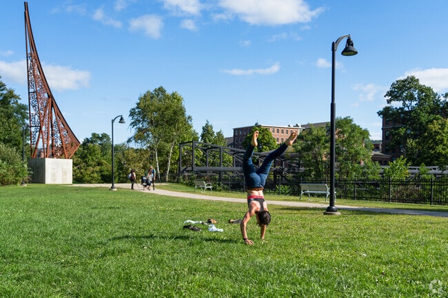 A person does a handstand on a green space along the Sugar River near East Side.