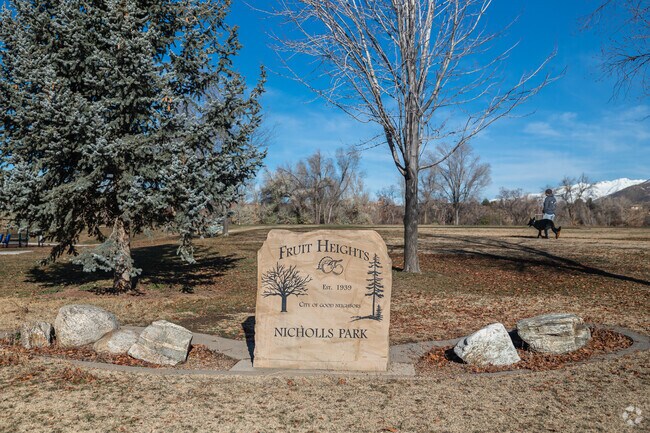 A man walks his dog behind a sandstone sign at Nicholls Park in Fruit Heights.