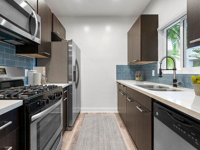 Blue tiled kitchen with granite countertop and stainless steel fridge, microwave, and fixtures.