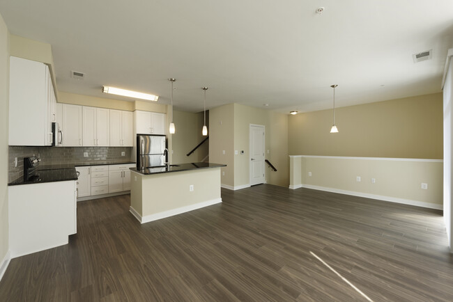 Townhome living area and open concept kitchen with granite countertops and tile backsplash, white shaker cabinetry, stainless steel appliances and hard surface flooring