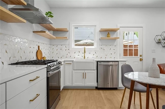 Open shelving system, light wood shelves, white cabinetry and countertops, & ample storage space.