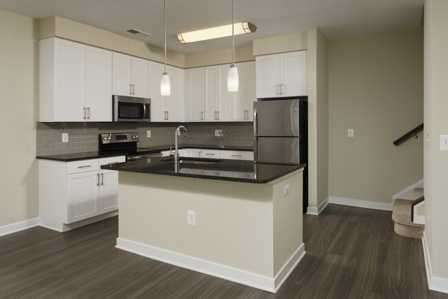 Townhome open concept kitchen with granite countertops and white shaker cabinetry, kitchen island, stainless steel appliances and hard surface flooring