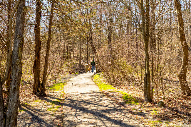 A person walks their dog along the tree-covered trails at Lisbon Meadows Park.