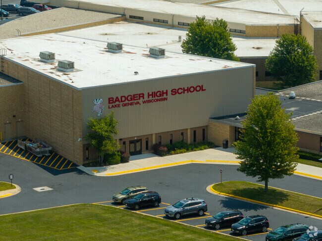 Main entrance of Badger High School with red signage and parked cars in Lake Geneva.