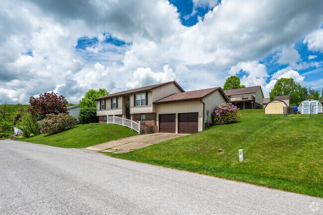 A bi-level home with a two car garage sits off the road on a slight rise.