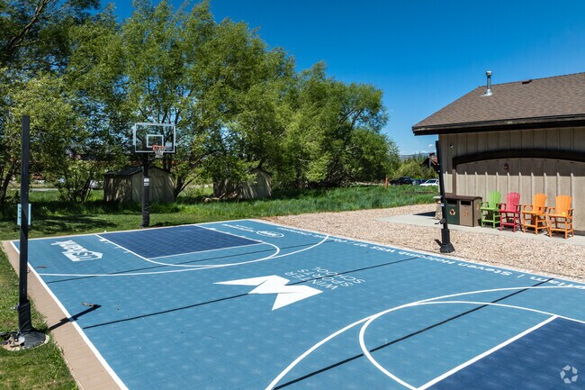 A blue outdoor basketball court contrasts green trees at The Winter Sports School.