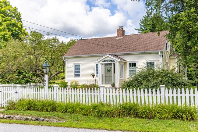 A well-maintained Cape Cod inspired home in Sutton, NH with a white picket fence.