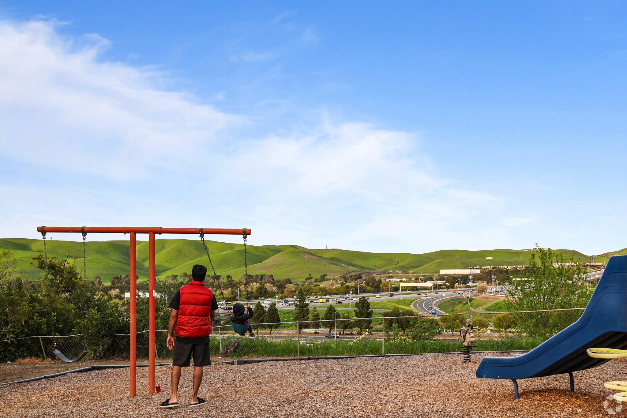 A man pushes his son on the swings at Bayview Circle Park, with Sun Terrace hills in view.