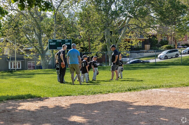 Young players huddle with coaches at Lindsey Gardens Park before a summer baseball game.