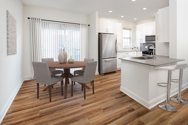 Kitchen and dining with white cabinetry, grey quartz countertops, grey tile backsplash, stainless steel appliances, and hard surface flooring