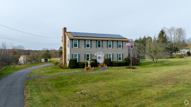 A colonial style home with solar panels has a green lawn and great sunlight in East Brookfield.