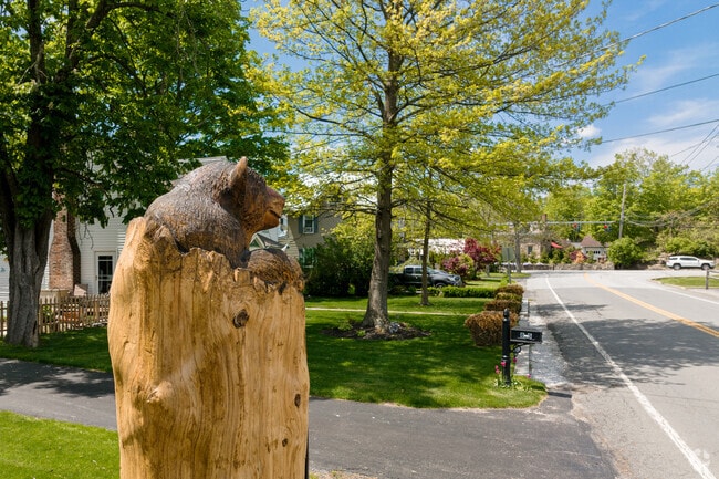 A charming roadside view in Wallkill Town featuring a hand-carved bear sculpture and tree-lined streets.