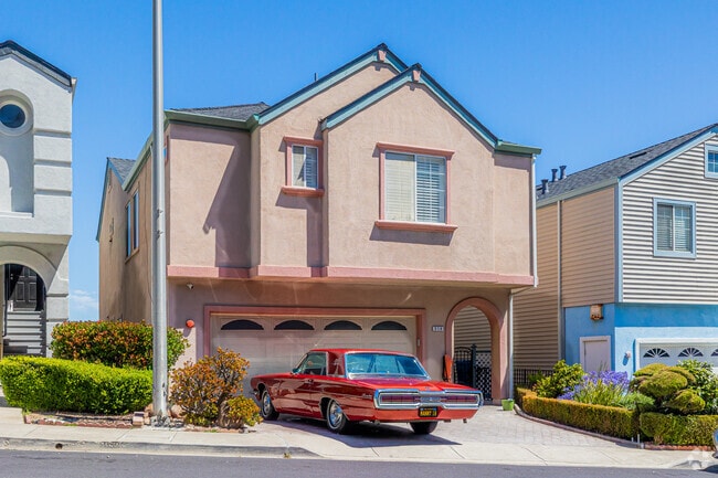 A classic red hot rod sits in front of a pastel-colored split-level home in Bayshore.