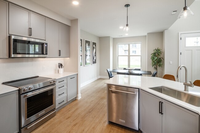 Signature Collection Townhome kitchen with upgraded stainless steel appliances, white quartz countertops and backsplash, grey cabinetry, hard surface flooring, and pendant lighting.